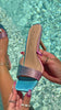 Video of model holding multi color embellished mid high heel by the pool
